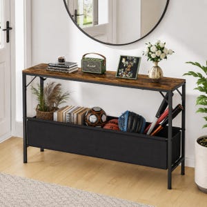 May include: A rectangular console table with a dark brown wood-grain top and a black metal frame. The unit features a lower black fabric storage bin containing books, a soccer ball, a basketball, a baseball glove, and several baseball bats.