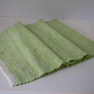 May include: A green and white woven placemat with a white border. The placemat is folded in thirds.