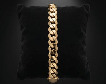 May include: A gold-toned metal chain bracelet featuring thick, interlocking curb links with a polished, reflective surface. The bracelet is displayed vertically, showcasing a uniform, heavy-duty design with a secure, integrated clasp at the base.