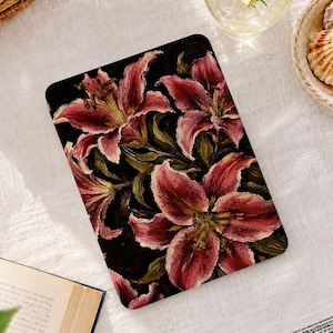 Puede incluir: Una funda rectangular para tableta o lector electrónico con un estampado detallado al estilo de pintura al óleo de lirios de color rojo oscuro y rosa con follaje verde oscuro sobre un fondo negro sólido. El diseño floral cubre toda la superficie.