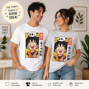 May include: A white t-shirt and a light gray t-shirt, each featuring a rectangular graphic of a smiling anime character with spiky black hair in an orange gi, accompanied by Japanese text and a speech bubble with the word "ニコッ".