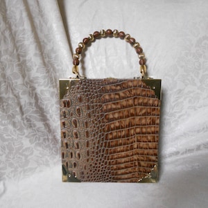 May include: A brown crocodile-embossed clutch purse with a gold frame and a beaded handle.