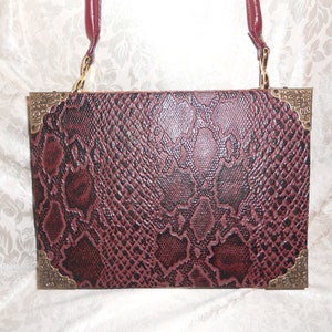 May include: A burgundy snakeskin clutch purse with gold-toned hardware and a chain strap.