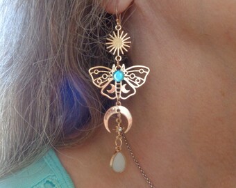 Puede incluir: Pendientes dorados con temática celestial. Los pendientes presentan un sol, una polilla con una piedra turquesa, una luna creciente y un dije en forma de lágrima. Los pendientes son colgantes y ornamentados.