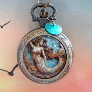 Op de afbeelding: Antieke bronzen zakhorlogehanger met een illustratie van een zeemeermin. Het horloge heeft een turquoise bedel en een gedetailleerde rand. De zeemeermin heeft lang bruin haar en een vissenstaart. De achtergrond is een blauwe oceaanscène.
