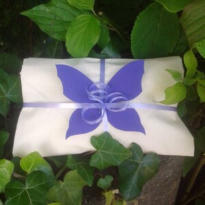 May include: A white gift bag with a purple butterfly cutout and a purple ribbon tied in a bow.