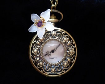 May include: A gold pocket watch with an ornate design and a white flower charm. The watch face is white with black hands and the word "QUARTZ" printed on it.