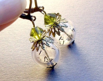 May include: A pair of dangle earrings with clear glass orbs containing dandelion seeds. The orbs are accented with gold filigree and green crystal beads.