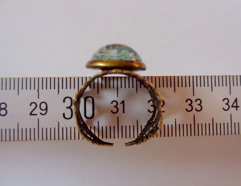 May include: A gold-toned adjustable ring with a blue and white glass cabochon. The ring is shown on a ruler, measuring approximately 30 mm in diameter.