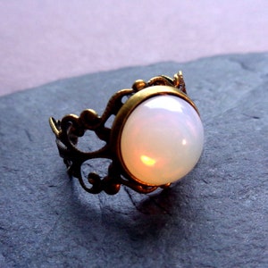 Op de afbeelding: Een ring met een witte opaal en een sierlijke messing setting. De ring heeft een delicaat, ingewikkeld ontwerp.