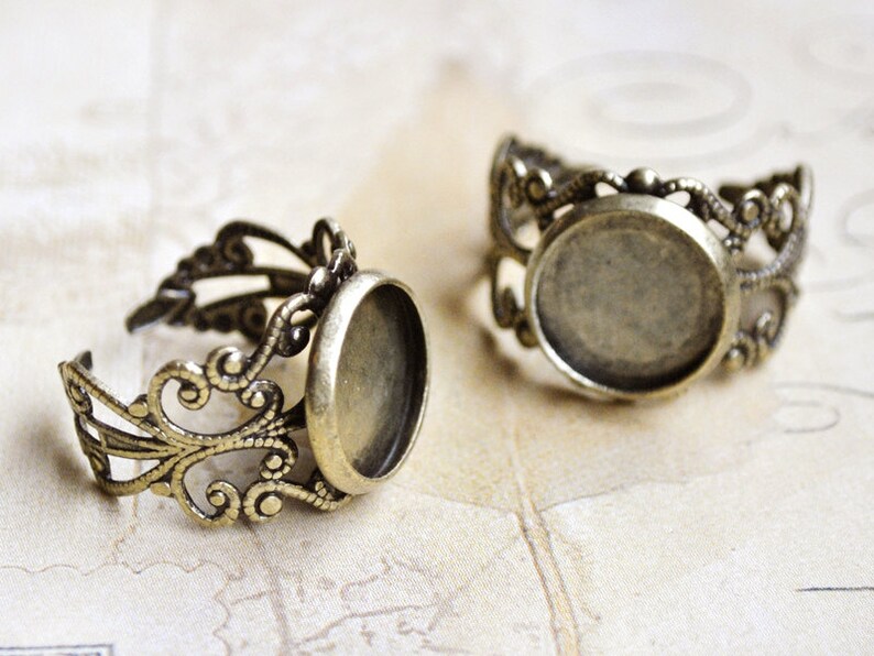 May include: Two antique gold-toned rings with a round, open bezel setting. The rings are made of filigree metal with a delicate, ornate design.