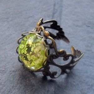 May include: A bronze ring with a delicate filigree design and a round green glass cabochon featuring pressed green flowers.