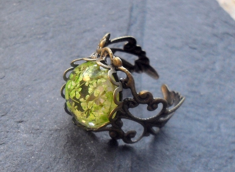 May include: A bronze ring with a delicate filigree design and a round green glass cabochon featuring pressed green flowers.