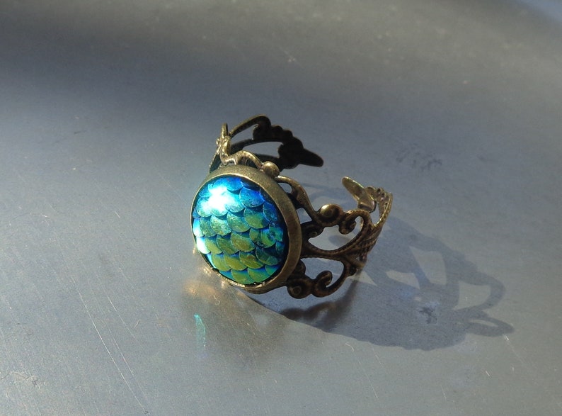 May include: A bronze ring with an ornate design and a round, iridescent blue and green gemstone with a scale pattern.