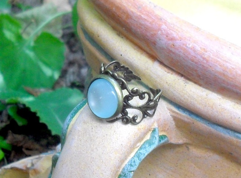 Op de afbeelding: Een ring met een lichtblauwe cabochon-steen gezet in een filigraan ontwerp van brons.