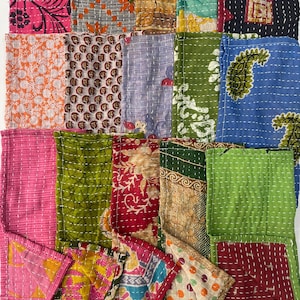 May include: A collection of rectangular fabric swatches featuring various patterns and colors, including pink, orange, green, blue, and black. Each piece is stitched with white thread in a running stitch pattern, creating a quilted texture.