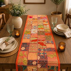 May include: A rectangular table runner featuring a patchwork design of various fabric squares in vibrant colors like orange, pink, green, and blue. The runner is decorated with intricate embroidery, small fabric flowers, and beads, finished with a bright orange border.