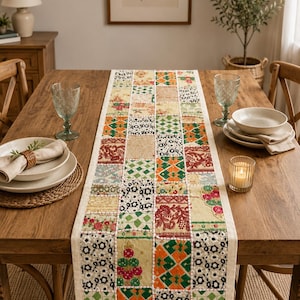 May include: A rectangular table runner featuring a patchwork design of various fabric squares. The squares display diverse patterns including floral motifs, geometric shapes, and intricate embroidery in shades of red, green, orange, and cream.