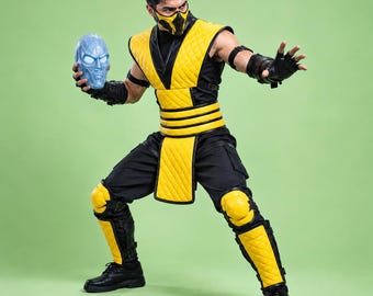 May include: A yellow and black quilted costume featuring a sleeveless vest, matching pants, shin guards, and knee pads. The outfit includes a yellow and black face mask and black gloves. A light blue, textured, human-like skull mask is held.