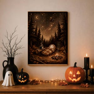 Puede incluir: Una impresión de arte mural enmarcada que representa a un personaje de dibujos animados durmiendo en un saco de dormir a cuadros junto a una fogata en un bosque oscuro bajo un cielo estrellado con una luna creciente, junto a un jarrón negro.