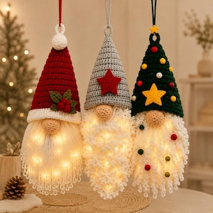 May include: Three hanging gnome ornaments with crocheted hats in red, gray, and dark green. Each gnome features a beige nose, a long white yarn beard illuminated by internal warm LED lights, and decorative accents including stars, berries, and small colorful spheres.