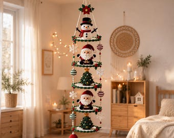 May include: A vertical hanging mobile featuring five stacked circular tiers decorated with crocheted Christmas figures including a snowman, two Santa Clauses, and two Christmas trees, accented with red and green beads and white snowflakes.