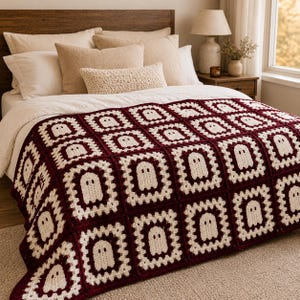 May include: A crochet blanket featuring a repeating pattern of square motifs. Each square consists of a cream-colored ghost shape centered within a dark maroon border. The blanket is constructed from individual joined squares with a textured finish.