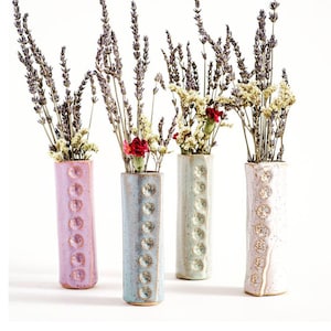 May include: Three ceramic vases with a textured, speckled finish and a row of raised circles. The vases are filled with dried lavender and a single red carnation.