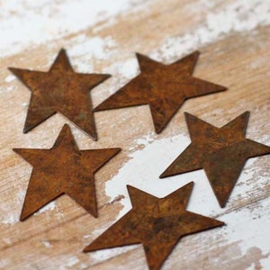 May include: Five rustic, metal, star-shaped ornaments in various sizes. The stars are a rusty brown color and have a distressed, vintage look.