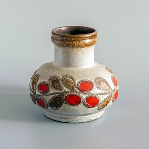 May include: A ceramic vase with a bulbous body and a short neck. The base color is a matte off-white with a textured finish. A horizontal band of repeating leaf-like shapes in vibrant red and earthy brown glazes encircles the center of the vase.