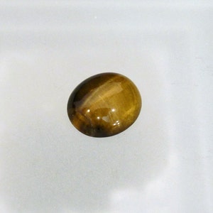 May include: A golden brown oval cabochon gemstone with a chatoyant effect, also known as tiger's eye.