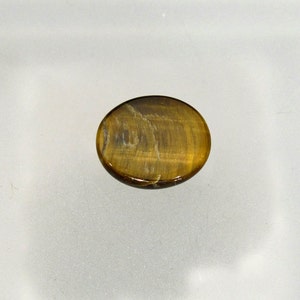 May include: A smooth, oval-shaped tiger's eye gemstone with a golden brown color and a subtle chatoyancy effect.
