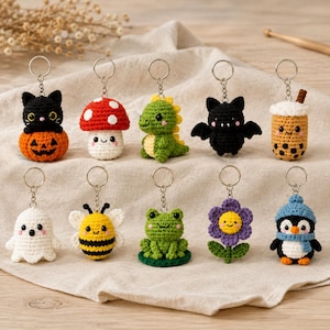 May include: A collection of ten small, handmade crochet keychains featuring various characters including a black cat on a pumpkin, a red mushroom, a green dinosaur, a black bat, a boba tea, a white ghost, a yellow bee, a green frog, a purple flower, and a penguin.