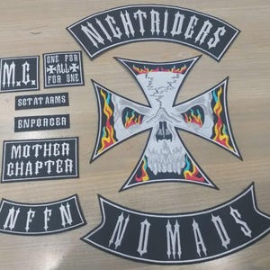 Puede incluir: Un conjunto de parches bordados en blanco y negro que incluye una gran cruz de hierro con un diseño de calavera y llamas, un rocker curvo Nightriders, un rocker Nomads y parches rectangulares más pequeños con M.C., One For All For One, Sgt At Arms, Enforcer, Mother Chapter y NFFN.
