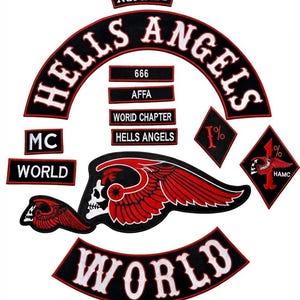 May include: A collection of black and red embroidered patches featuring the text HELLS ANGELS, NOMADS, WORLD, MC, AFFA, 666, and WORLD CHAPTER. The set includes a large winged skull emblem, a diamond-shaped 1% patch, and various rectangular labels.