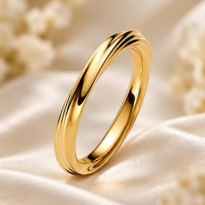 Peut inclure: Une bague en or poli dotée d'un anneau lisse et continu avec un design torsadé subtil et fluide, créant de légères ondulations sur la surface extérieure qui reflètent la lumière avec un éclat métallique brillant.