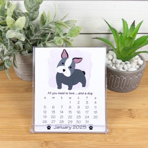 Könnte beinhalten: Ein Desktop-Kalender mit einer Cartoon-Illustration eines französischen Bulldoggen. Der Kalender ist für Januar 2025 und trägt den Text "All you need is love...and a dog".