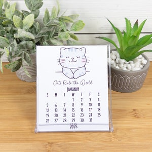 May include: A white desk calendar with a cartoon cat illustration and the text "Cat's Rule the World". The calendar shows the month of January 2025.