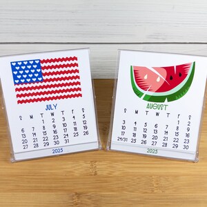 May include: Two small desk calendars with a white background. The July calendar features a red, white, and blue American flag with white hearts. The August calendar features a green watermelon slice with red flesh and black seeds. Both calendars have the year 2025 printed at the bottom.
