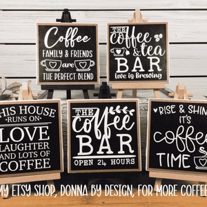 May include: Five black chalkboard signs with white lettering on wooden easels. The signs feature coffee-themed sayings, including "Coffee Family & Friends are the Perfect Blend", "The Coffee & Tea Bar Love is Brewing", "This House Runs on Love Laughter and Lots of Coffee", "The Coffee Bar Open 24 Hours", and "Rise & Shine It's Coffee Time".