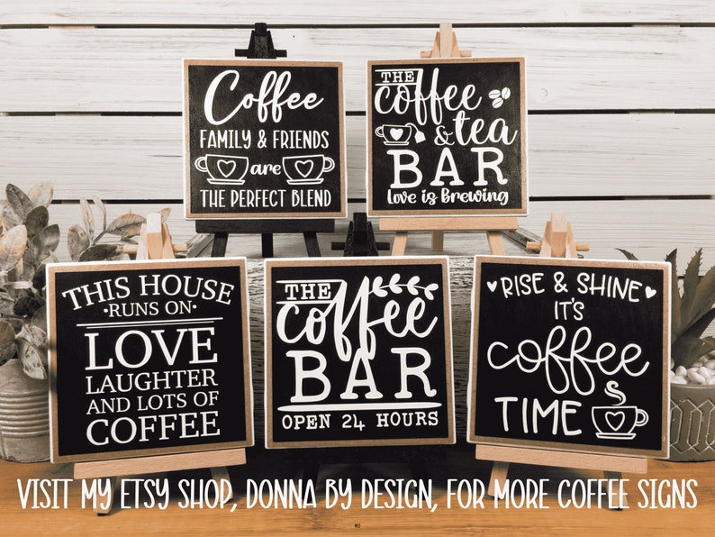 May include: Five black chalkboard signs with white lettering on wooden easels. The signs feature coffee-themed sayings, including "Coffee Family & Friends are the Perfect Blend", "The Coffee & Tea Bar Love is Brewing", "This House Runs on Love Laughter and Lots of Coffee", "The Coffee Bar Open 24 Hours", and "Rise & Shine It's Coffee Time".