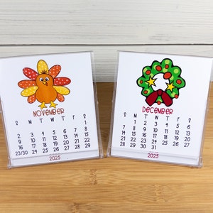 May include: Two small desktop calendars with a Thanksgiving turkey and a Christmas wreath design. The November calendar features a cartoon turkey with orange, yellow, and red feathers. The December calendar features a green wreath with red berries and a red bow. Both calendars are for the year 2025.