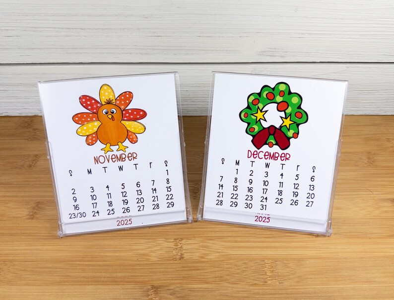 May include: Two small desktop calendars with a Thanksgiving turkey and a Christmas wreath design. The November calendar features a cartoon turkey with orange, yellow, and red feathers. The December calendar features a green wreath with red berries and a red bow. Both calendars are for the year 2025.