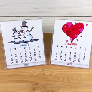 May include: Two small desk calendars with a winter and a Valentine's Day theme. The January calendar features a cartoon illustration of two snowmen. The February calendar features a cartoon illustration of a large red heart with smaller hearts around it. Both calendars are for the year 2025.