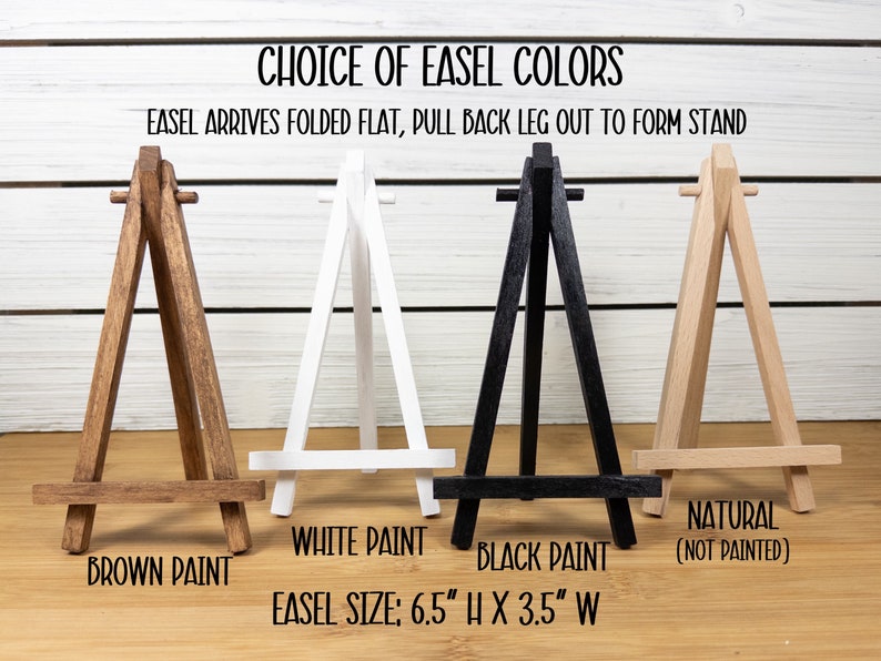 May include: Four wooden easels in different colors: brown, white, black, and natural. The easels are 6.5 inches tall and 3.5 inches wide. The text "Choice of Easel Colors" and "Easel arrives folded flat, pull back leg out to form stand" is at the top of the image.