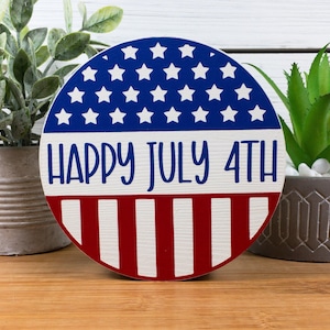 Könnte beinhalten: Ein rundes Holzschild mit einem rot-weiß-blauen amerikanischen Flaggenmuster. Das Schild trägt die Aufschrift "Happy July 4th" in weißen Buchstaben.