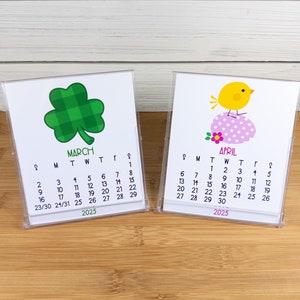 May include: Two small desktop calendars with a green shamrock and a yellow chick design. The March calendar has the dates 1-31 and the April calendar has the dates 1-30. Both calendars are for the year 2025.