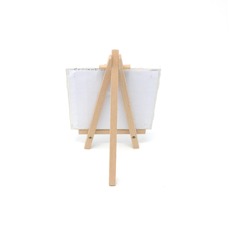 Puede incluir: Un peque&ntilde;o caballete de madera natural con un lienzo blanco. El caballete tiene un dise&ntilde;o de tres patas y est&aacute; hecho de madera de color claro. El lienzo es rectangular y parece estar en blanco. El caballete es adecuado para exhibir peque&ntilde;as obras de arte o fotos.