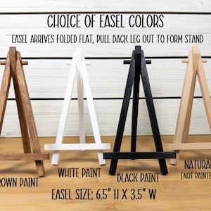 May include: Four wooden easels in different colors: brown, white, black, and natural. The easels are 6.5 inches tall and 3.5 inches wide. The text "Choice of Easel Colors" and "Easel arrives folded flat, pull back leg out to form stand" is at the top of the image.