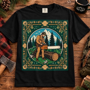 May include: A black t-shirt featuring a graphic print of a person in a cap and work clothes using a chainsaw on a log. The scene is set against a backdrop of mountains and pine trees, framed by a decorative border of orange leaves and vines.